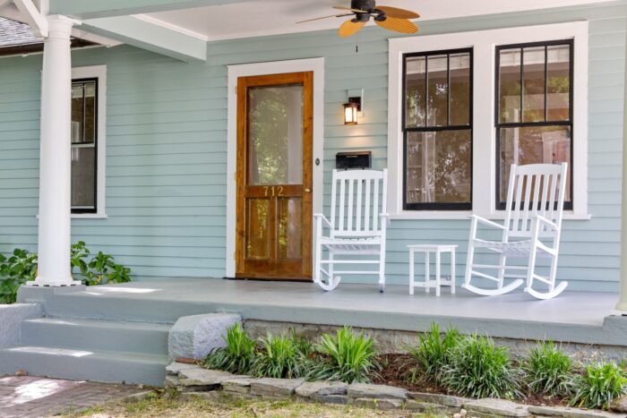 A Home With Pale Blue Siding And A Porch With White Rocking Chairs