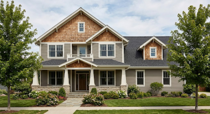 A two-story Craftsman home with gray horizontal siding, cedar shake gables, stone porch accents and a landscaped front yard.