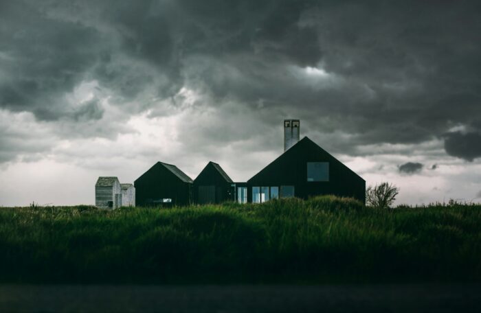 Dark storm clouds loom over a modern farmhouse as strong winds sweep across the grass.