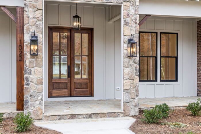 A contemporary home facade with vertical board-and-batten siding, stone trim, wooden double doors and lantern lighting