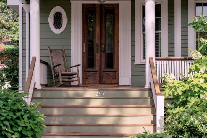 A front porch with green horizontal siding, a wooden door and white trim.