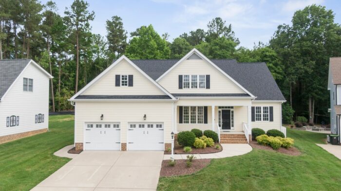 A home has beige siding, white trim, a two-car garage and a side sunroom addition.
