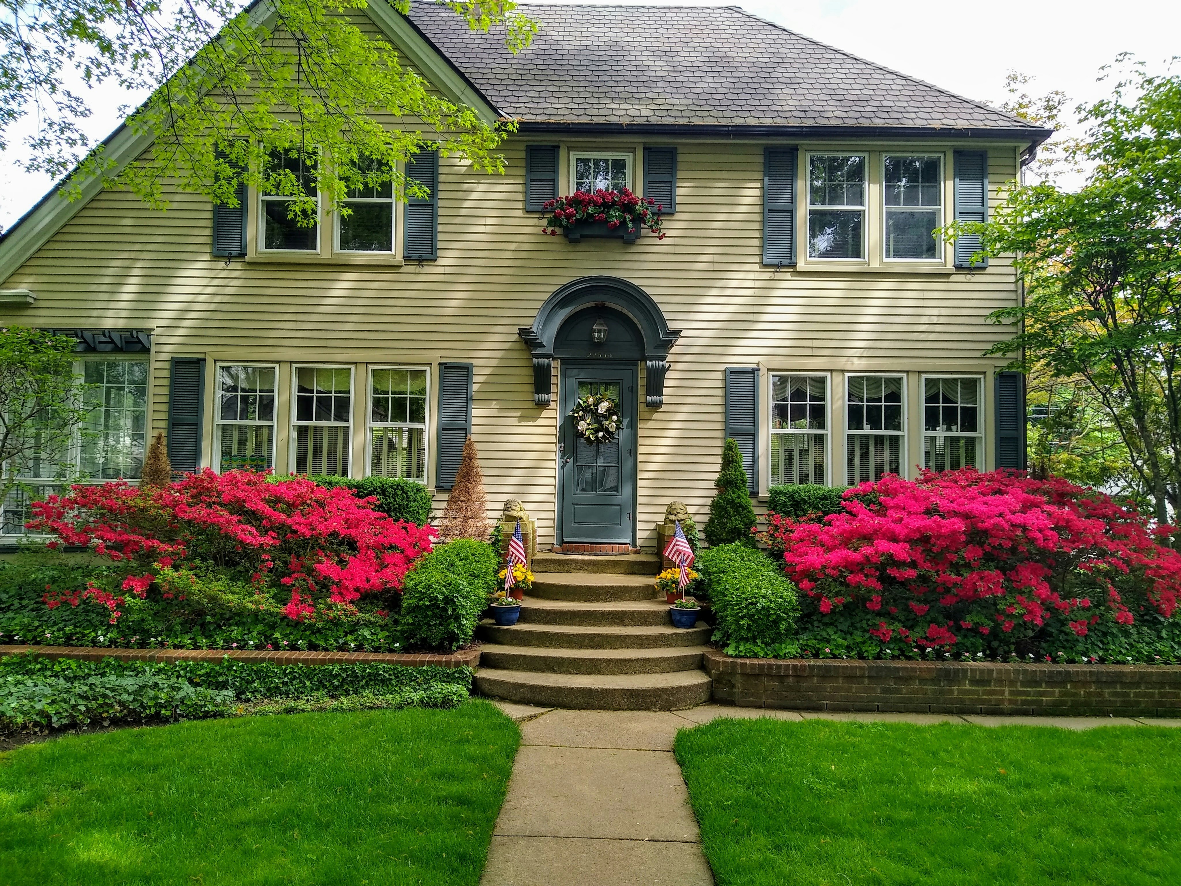 This image depicts a colonial-style home with dark green shutters and moulding above the front door.