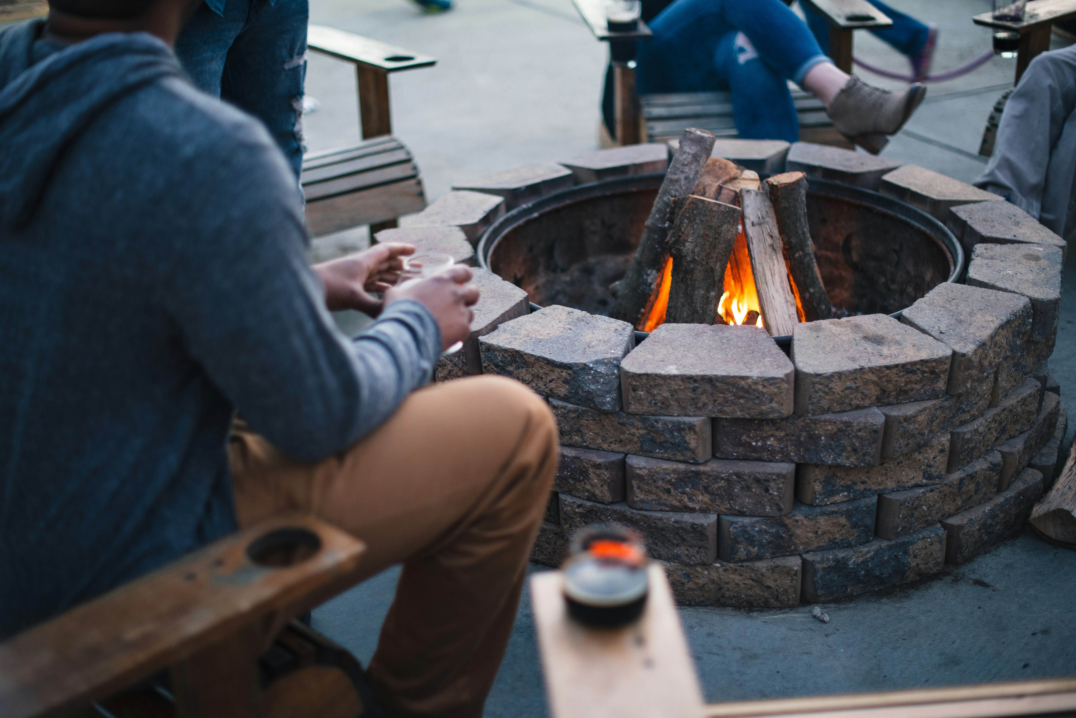 A person is sitting in a chair by a firepit. They are holding a drink.