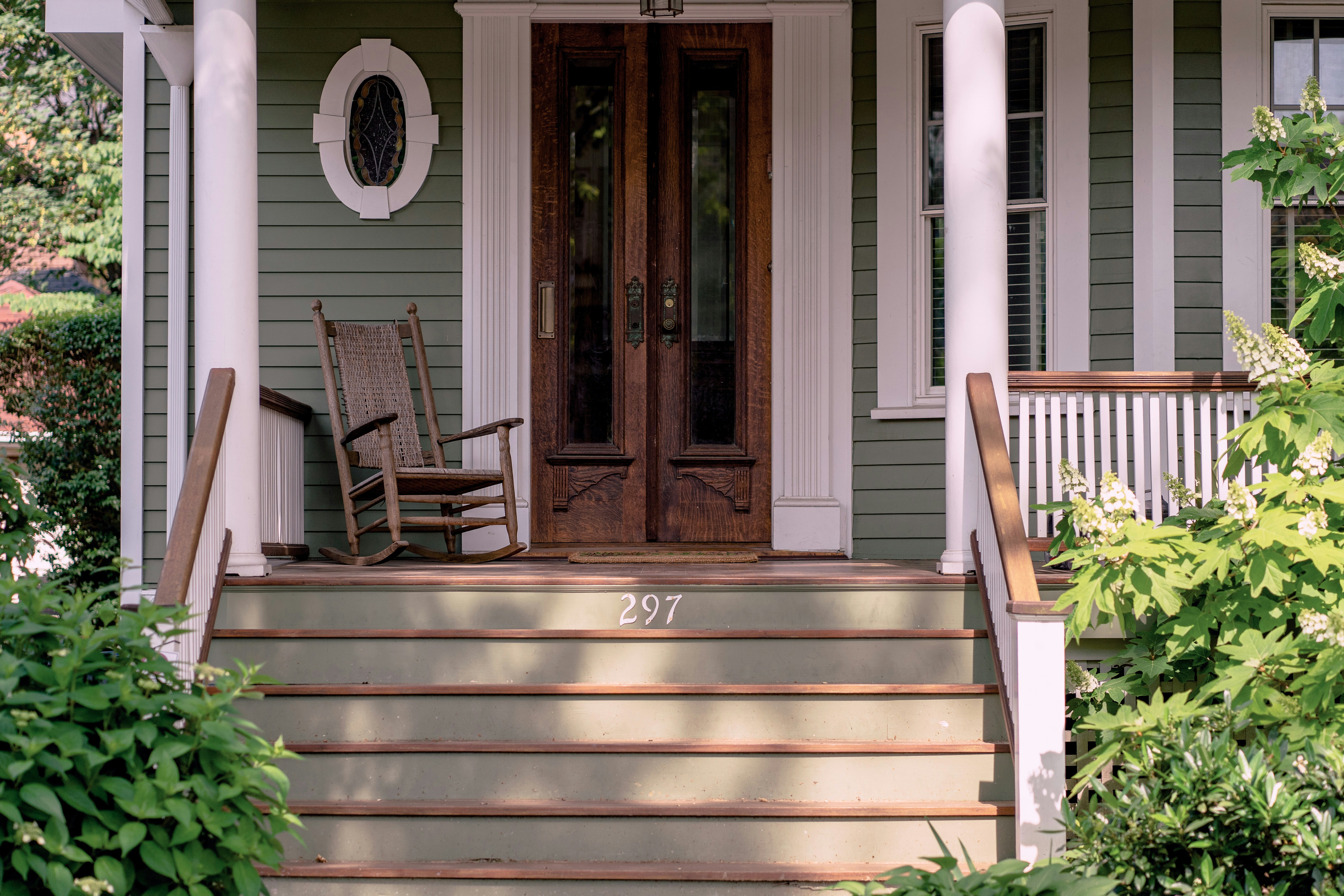 A front porch with green horizontal siding, a wooden door and white trim.