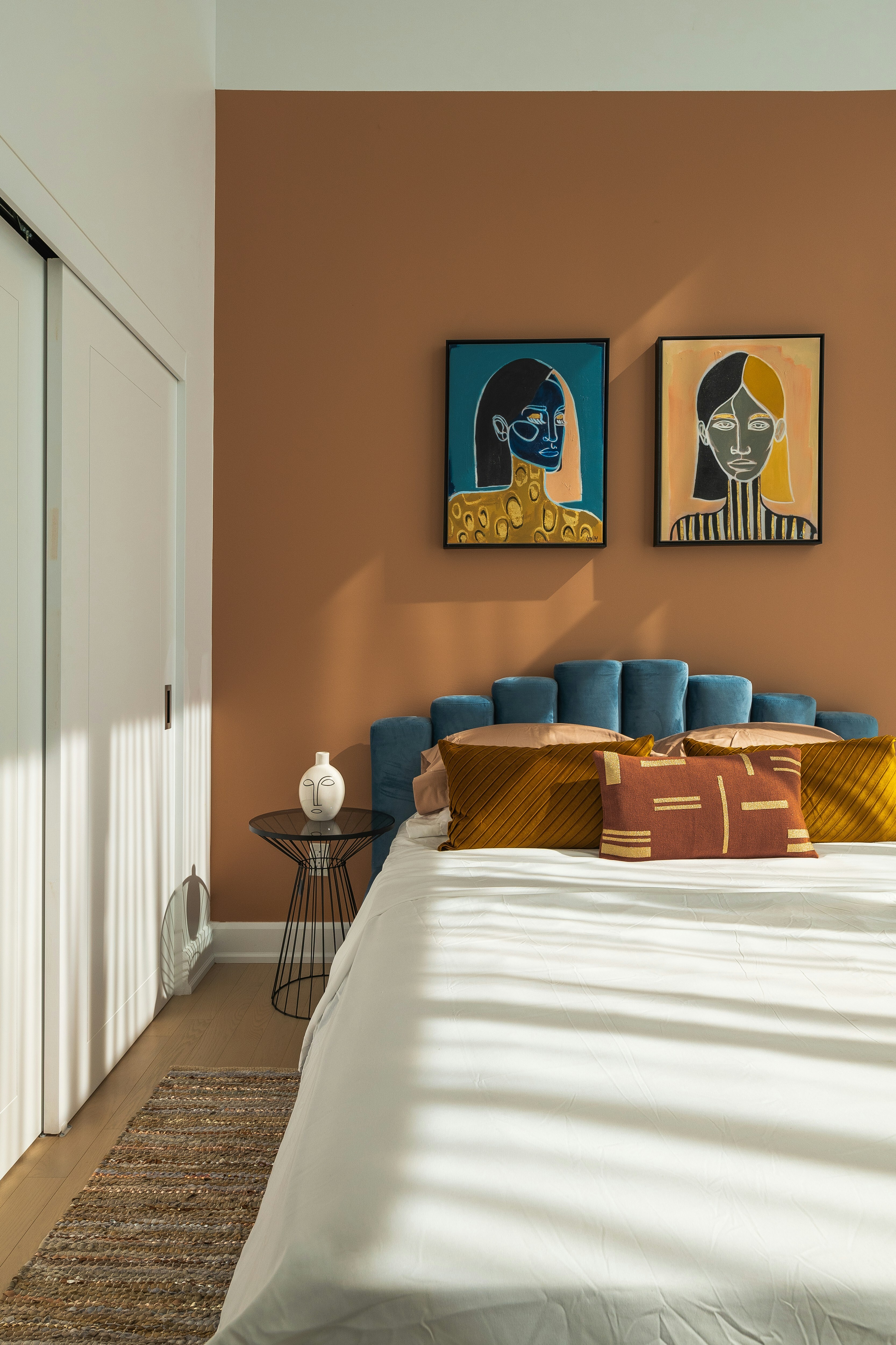 This image depicts a bedroom with a light brown wall. Unique artwork hangs above the bed.