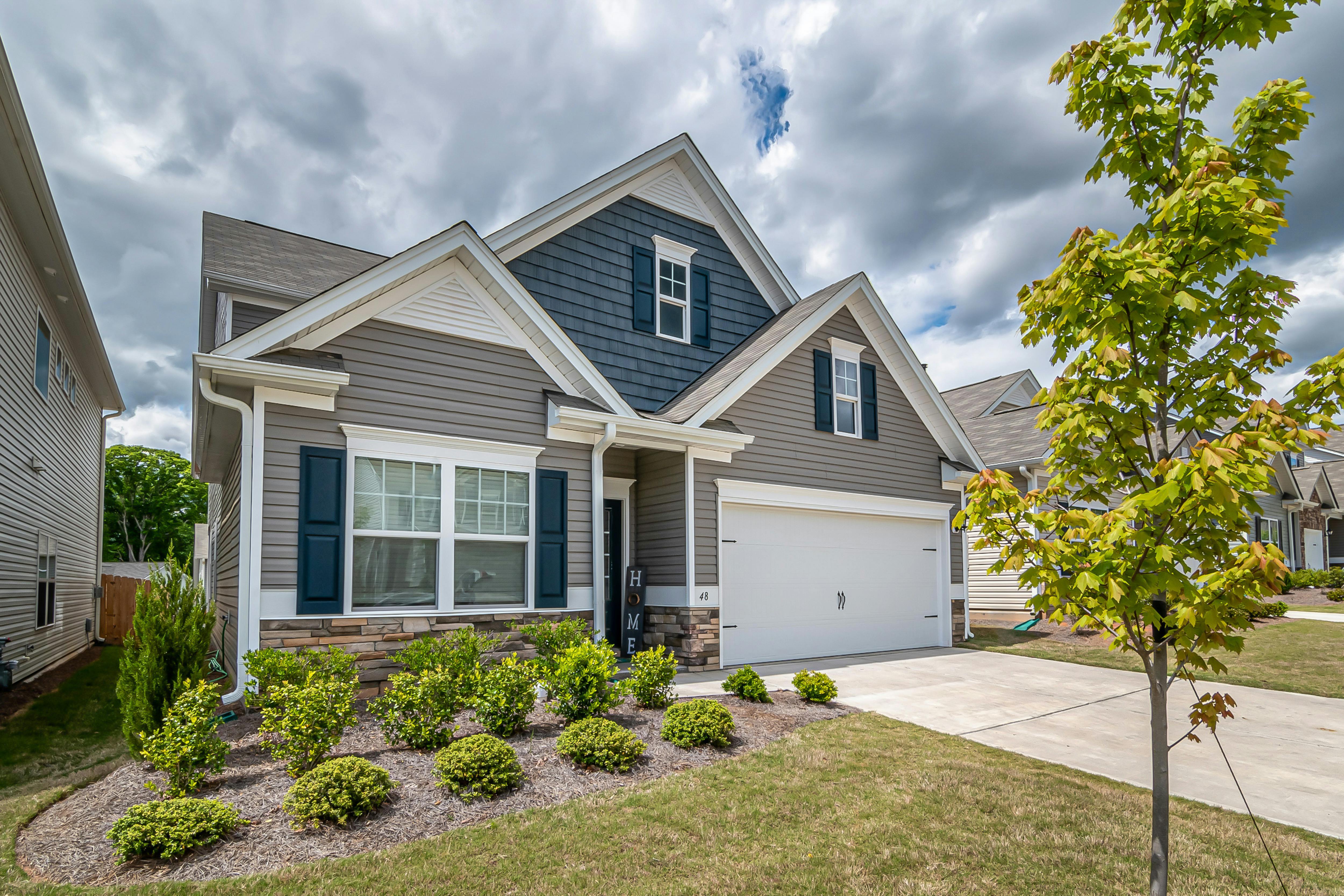 A beige and blue home has white trim and black shutters with a paved driveway leading to the garage.