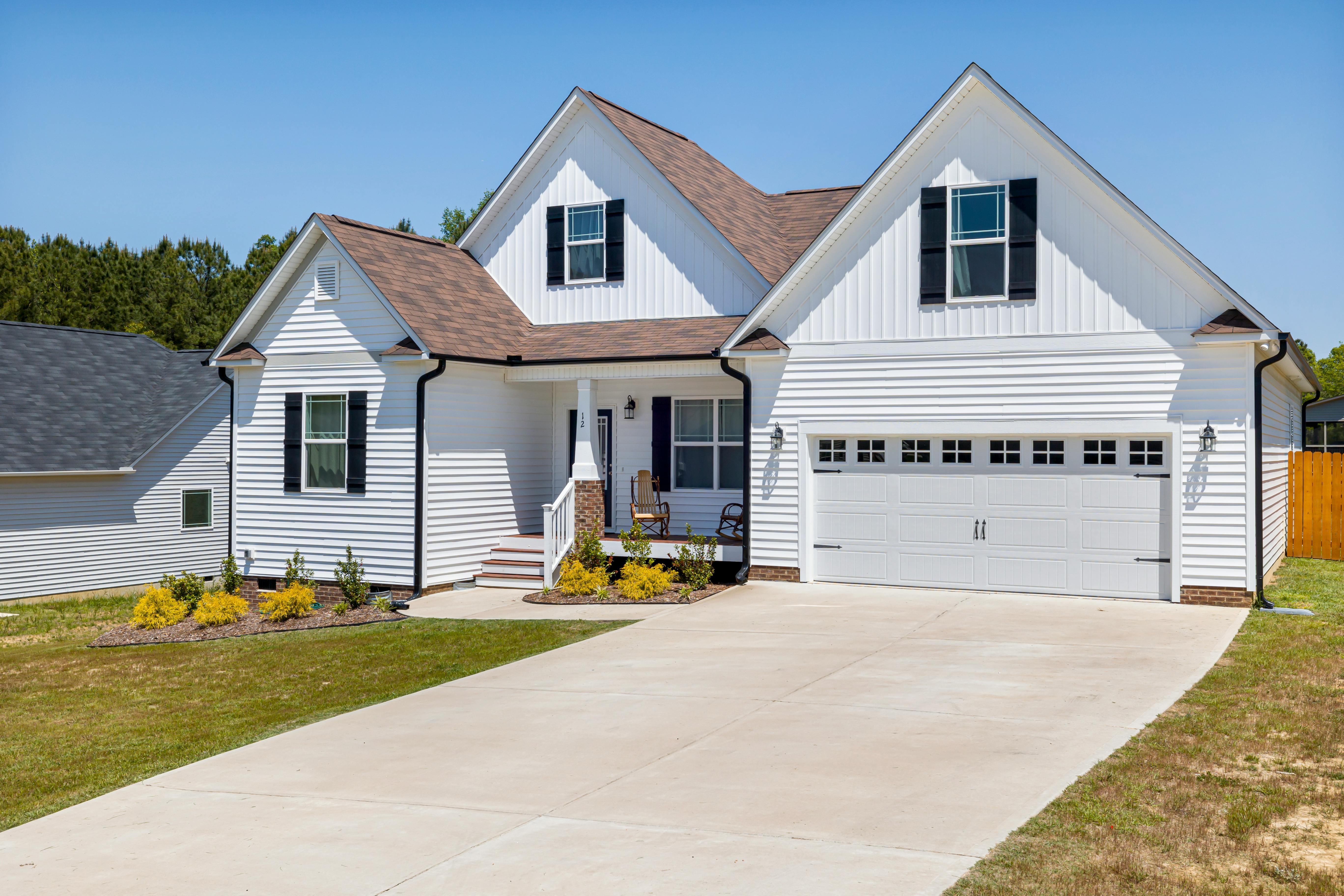 A white home with black gutters and shutters has the sun shining directly on the siding.