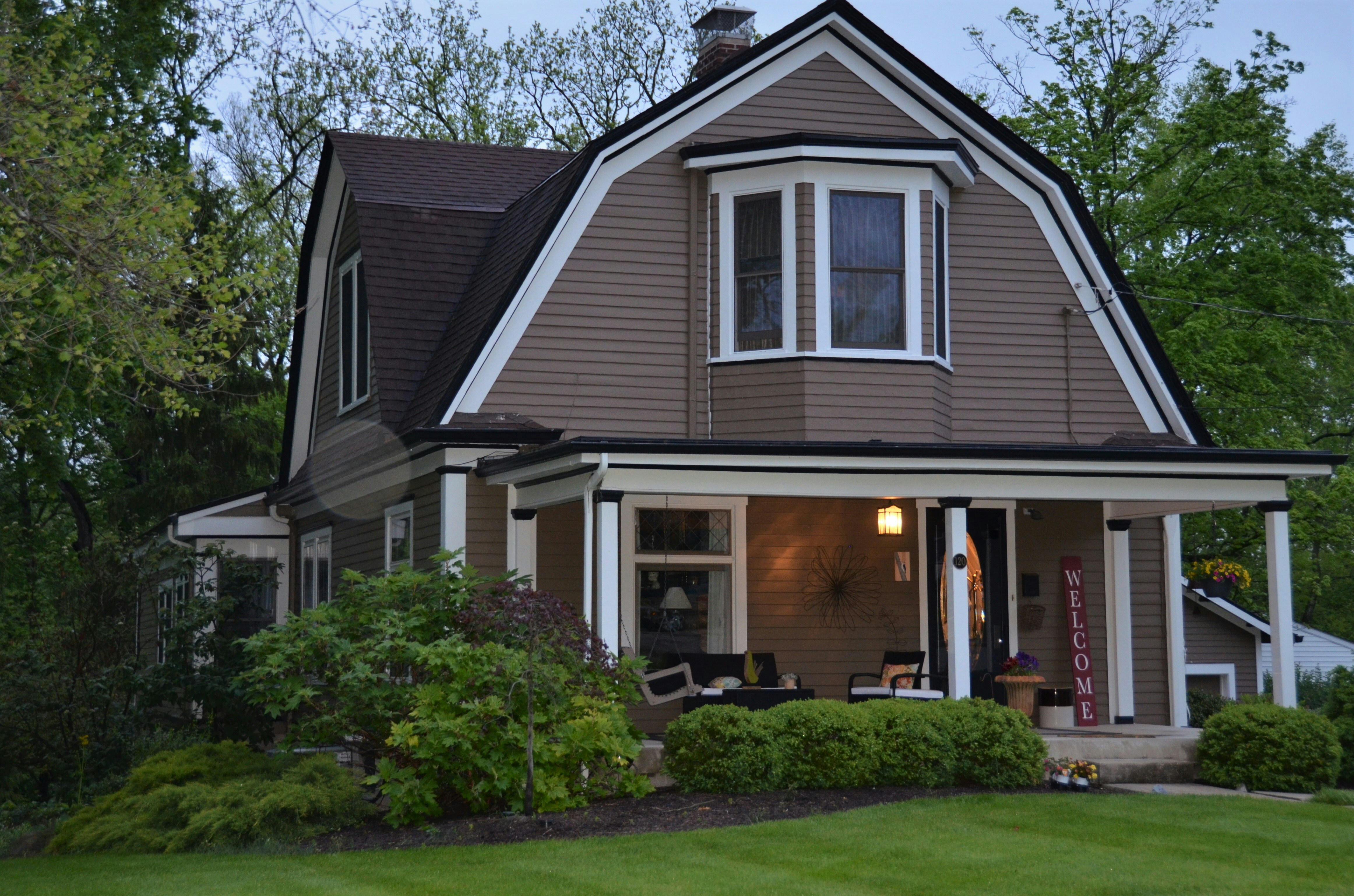 This image depicts a two-story house with a light brown siding and white trim.